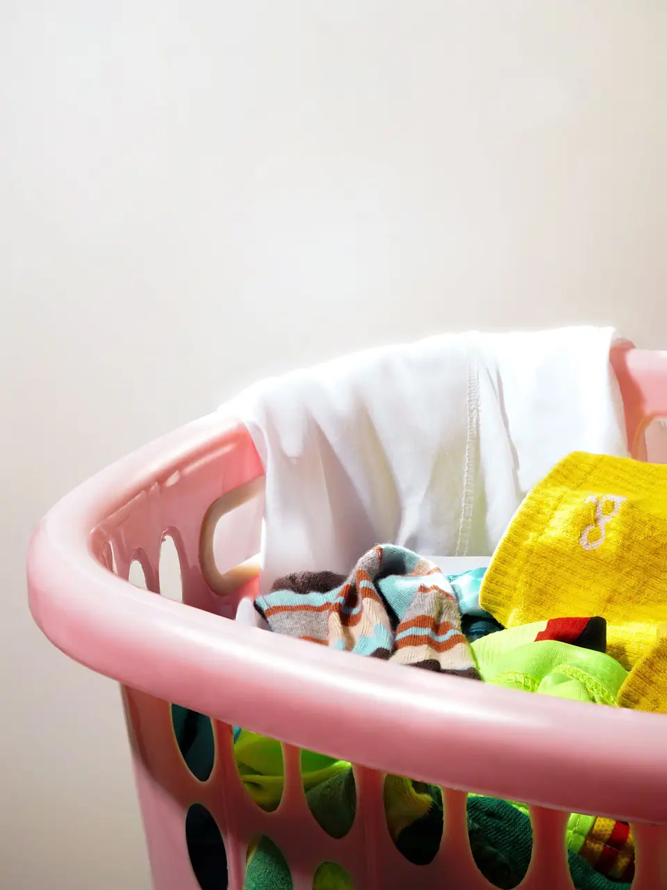 A pink laundry basket filled with colorful clothes. Bright and fresh household scene.