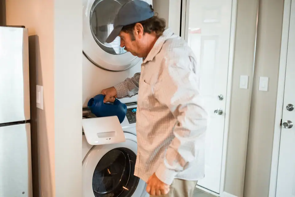 A man pouring liquid detergent into the dispenser drawer of a stacked washer