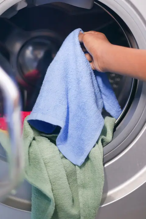 Close-up of a hand placing colorful towels into a front-loading washing machine.